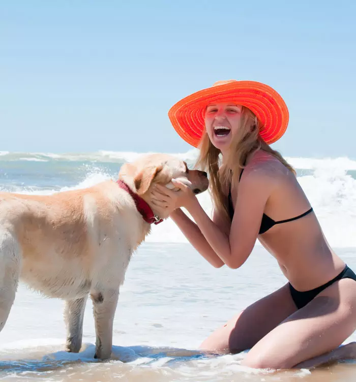 צעירה בביקיני שחור וכובע אדום משחקת על כלב על חוף הים