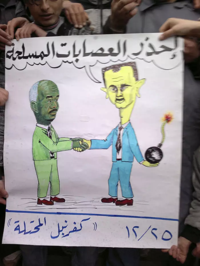 משתפים פעולה? שלט בהפגנה בסוריה המציג את בשאר אסד ומוחמד דאבי לוחצים ידיים