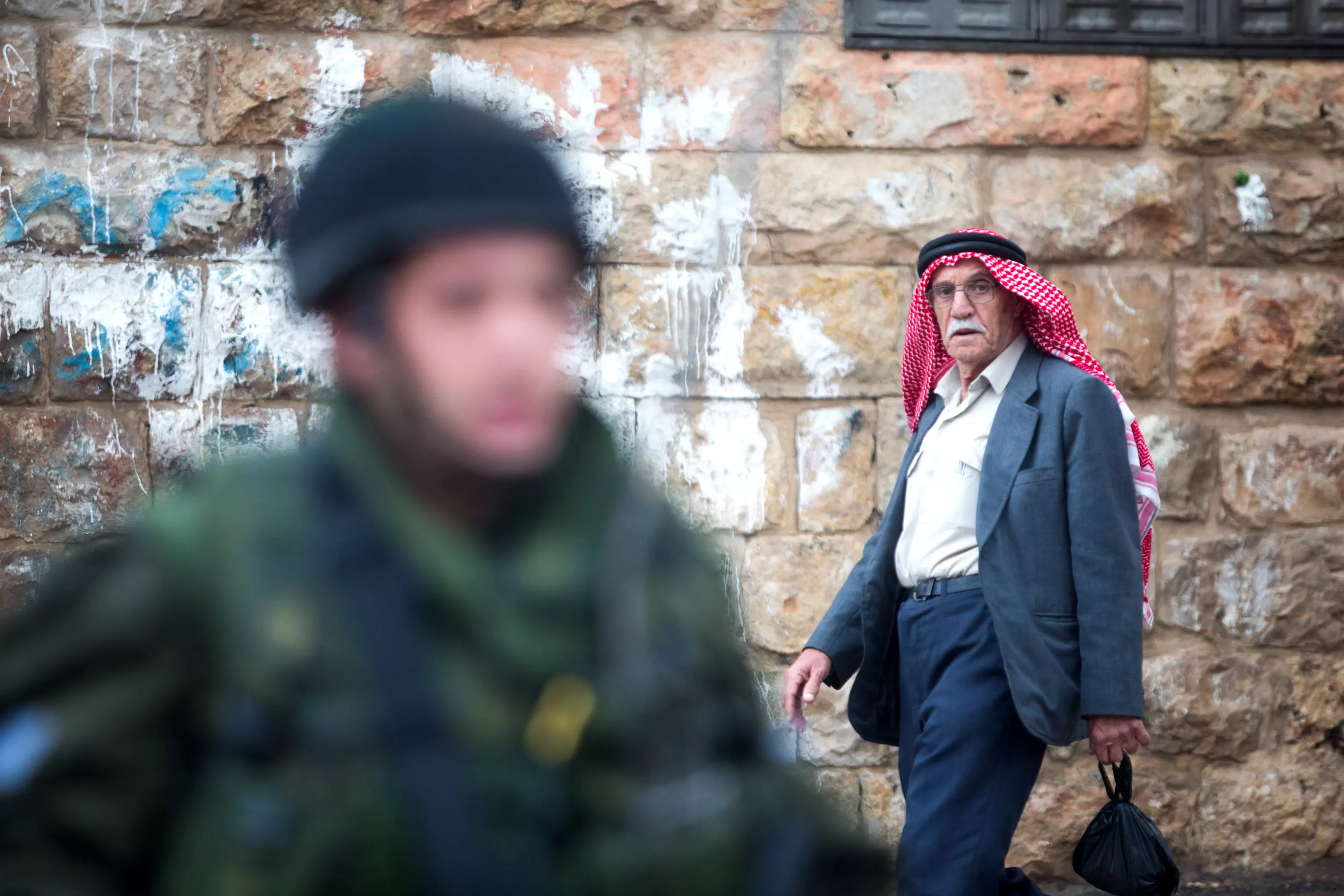 פלסטיני הולך ליד חייל צה"ל בעיר חברון