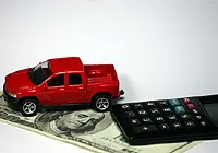 מכונית צעצוע מונחת מעל שטר כסף, לצד מחשבון כיס