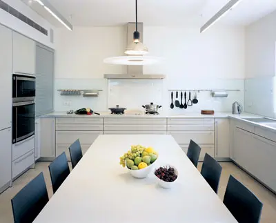 המטבח, עם חיפוי זכוכית לקירות לאורך משטח העבודה, פלורסנטים בתקרה ושולחן לבן ארוך