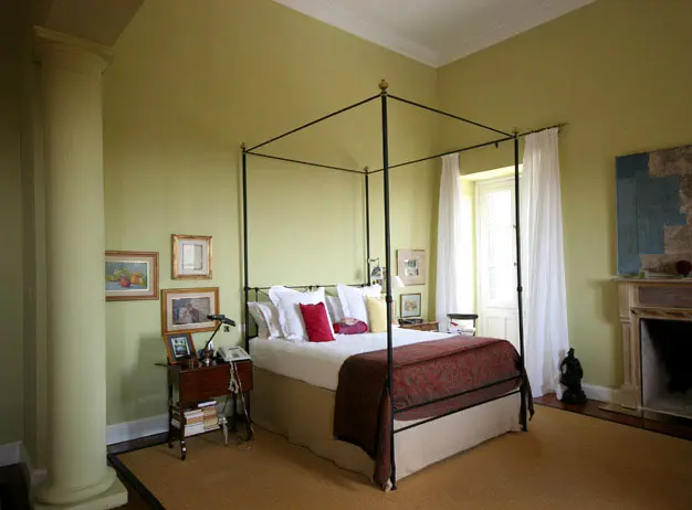חדר השינה. צבע הקיר מאיר את החדר ומדגיש את קווי מיטת הברונזה העטופה בסדיני פשתן