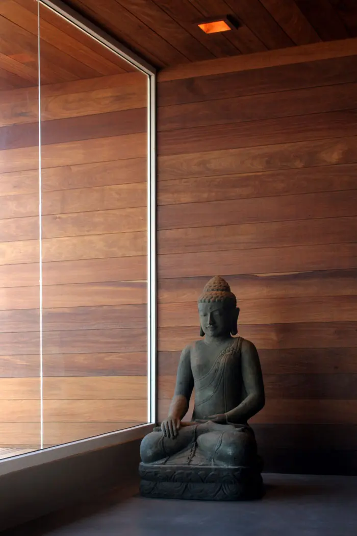 בכניסה לבית מוצב פסל בודהה עשוי אבן, על ריצפת בטון מוחלק ומאחוריו קיר עץ