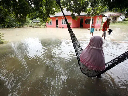 ילדה כפרית יושבת על ערסל ומסתכלת על משפחה היוצאתמביתה בעקבות הצפה, מלזיה