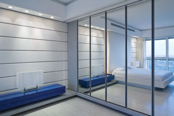 חדר השינה נשקף בדלתות ארון הקיר הנראה כמונח על מדף שמכתר את כל החדר