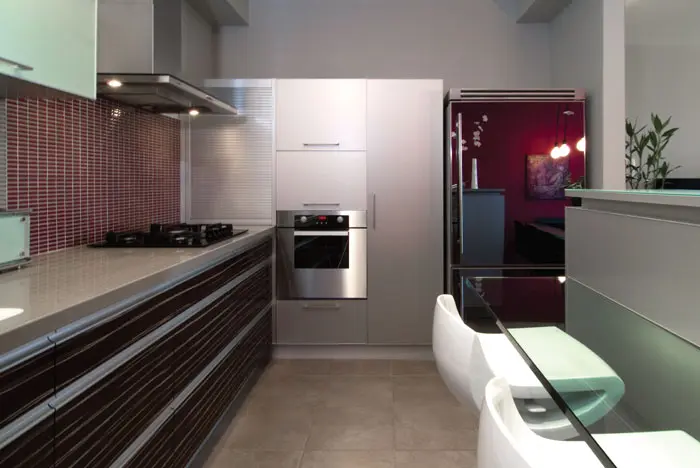 בקצהו המוארך של המטבח, דלתות המקרר עם אפקט המראה בהן משתקפת פינת האוכל