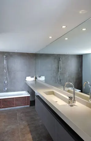 חדר הרחצה עם לייסטים בתחתית האמבטיה משטח כיור, הנמשך מקיר לקיר בהתאם לציר המבט, ומראה שמייצרת הכפלה והגדלה של החדר הקטן לכיוון השני