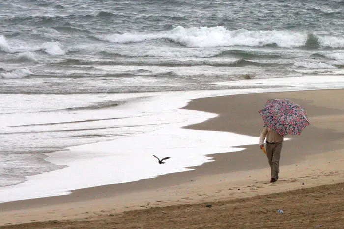 גבר הולך על שפת הים עם מטריה