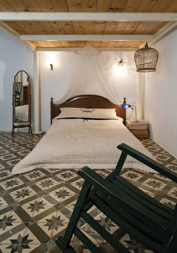 בין קורות ברזל ולוחות עץ פשוט, לבין רצפה אפורה מקורית וישנה ניצבת המיטה עם כילה רומנטית המדגישה את ראש המיטה המסוגנן