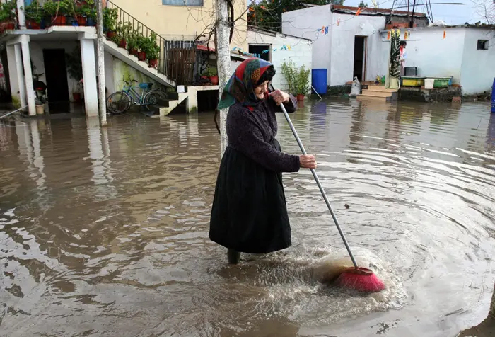 אשה אלבנית מפנה מי גשם שהציפו את ביתה