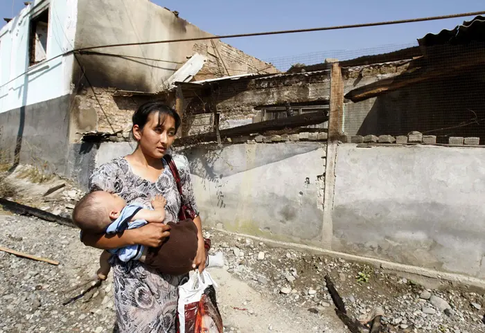 אוזבקית ותינוקה חולפים על פני בית באוש שנשרף