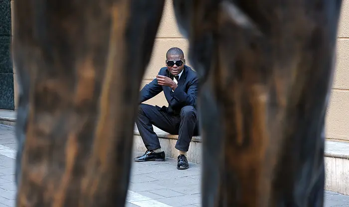איש דרום אפריקאי יושב ליד הפסל של נלסון מנדלה