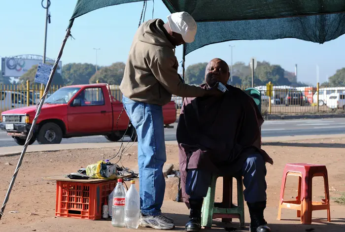 אדם דרום אפריקאי מגלח אדם אחר במכונת גילוח