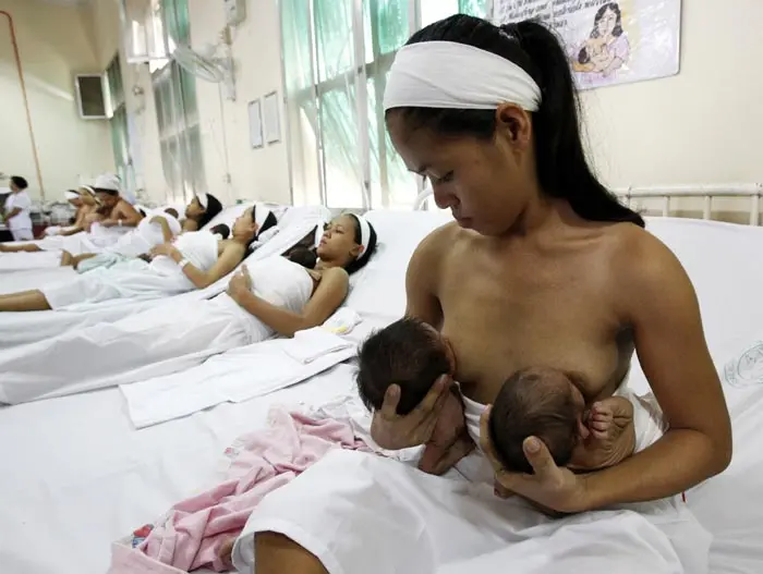 אישה בפיליפינים מניקה את התאומים שלה