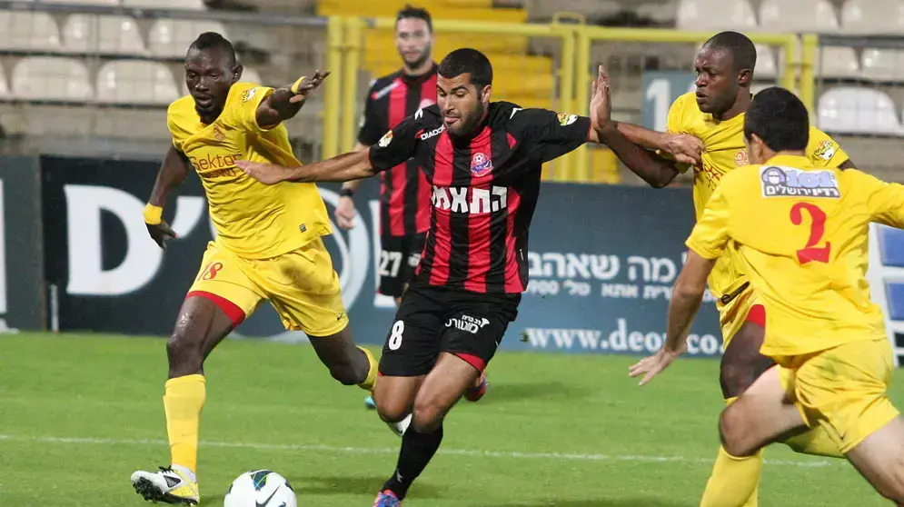 הישאם כיוואן שחקן הפועל חיפה (אמצע) מול ג'ואון אושאניווה שחקן מ.ס. אשדוד