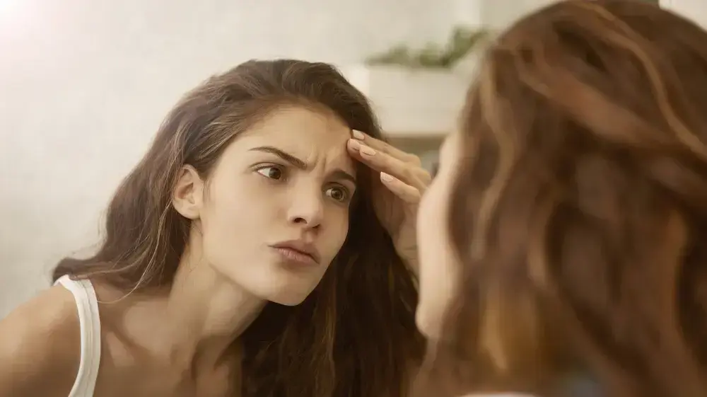אישה צעירה מסתכלת במראה ובוחנת את הקמטים שלה