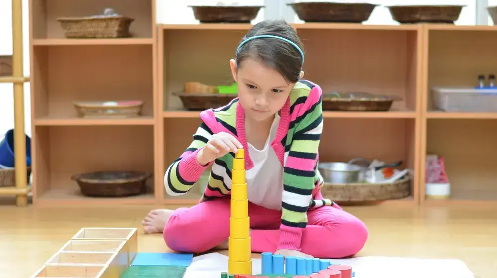 ילדה משחקת בצעצועי עץ על שטיחון בחדר משחקים