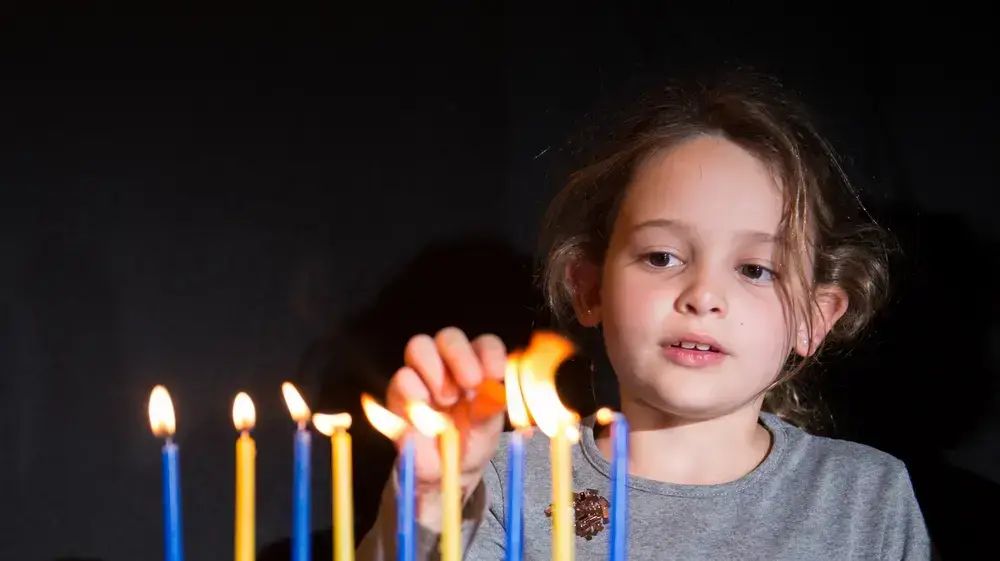 ילדה מדליקה נרות חנוכה בחנוכיה - חנוכה 2023