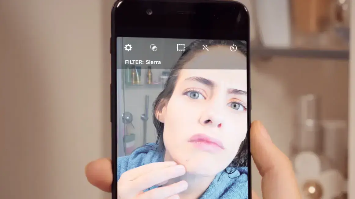 בחורה מביטה בפניה באמצעות הסמארטפון ומגלה פצעון