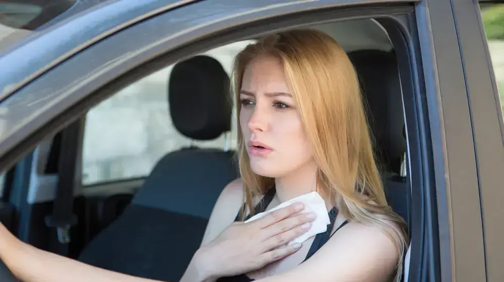 אישה נוהגת במכונית ומנגבת זיעה אישה נוהגת במכונית ומנגבת זיעה