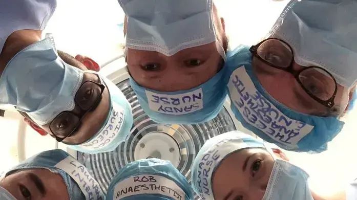 צוות חדר ניתוח עם כובעים שעליהם שמותיהם ותפקידיהם