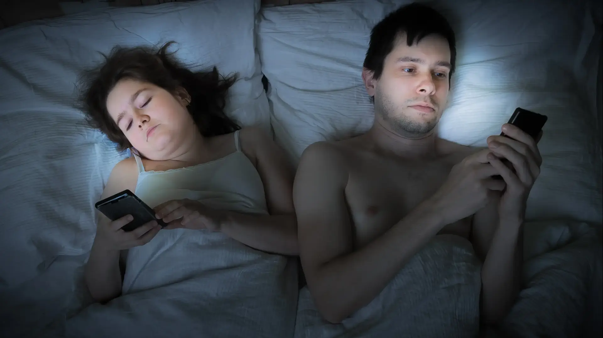 בני זוג במיטה עם טלפונים ניידים