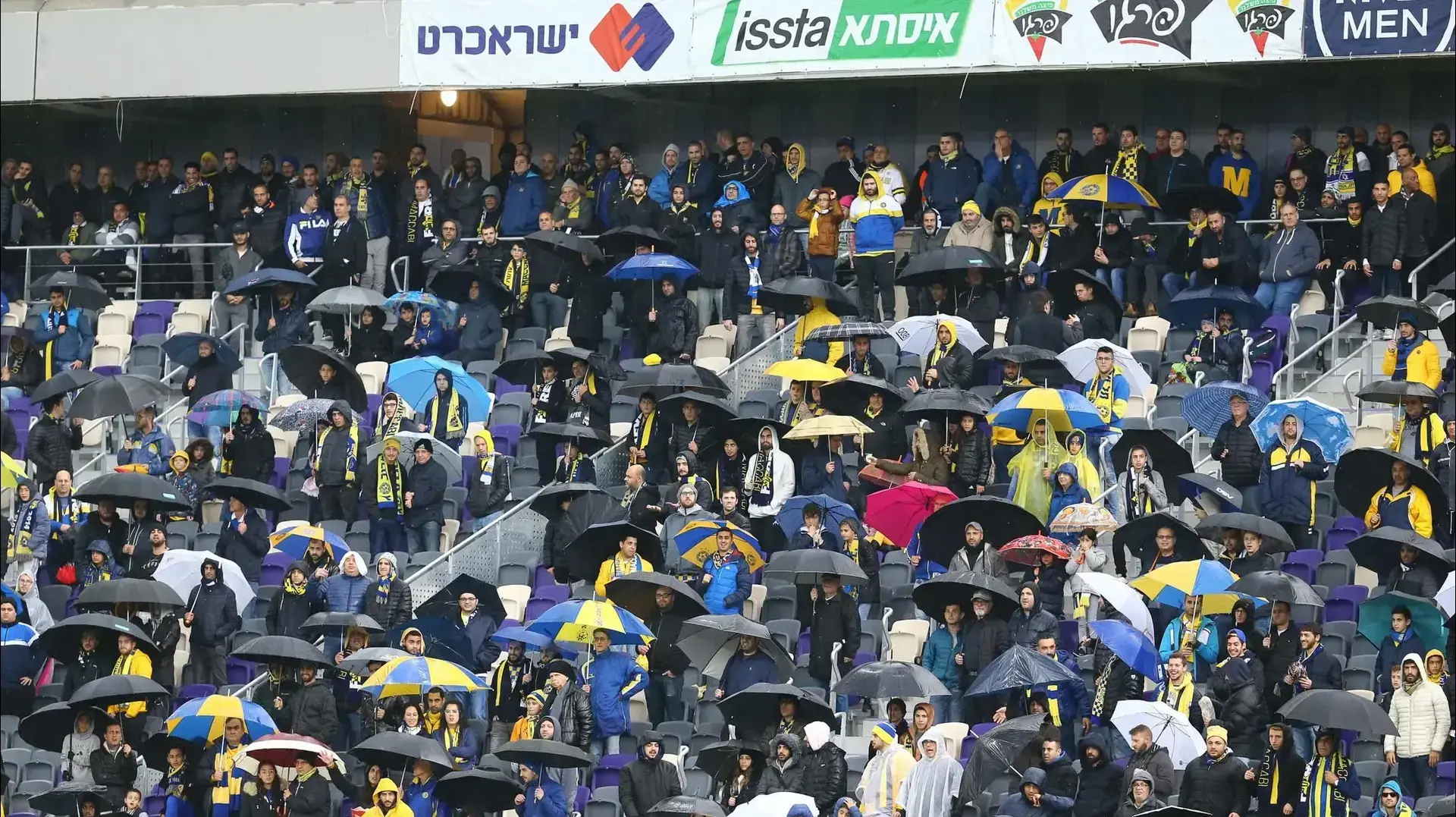 אוהדי מכבי תל אביב עם מטריות, גשם, אצטדיון בלומפילד