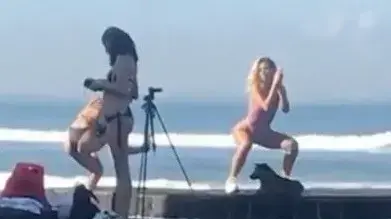 דוגמנית מצטלמת על החוף לצד קבוצה של נשים מקומיות המתכוננות לקיום טקס דתי