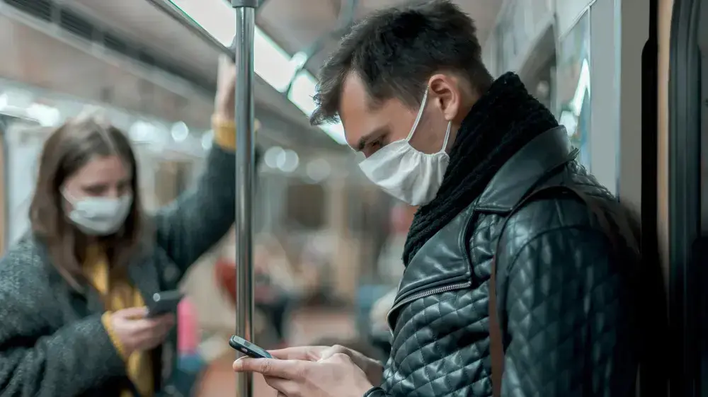 נוסעים ברכבת התחתית עוטים מסיכות פה ואף ומביטים בטלפונים הסלולריים שלהם
