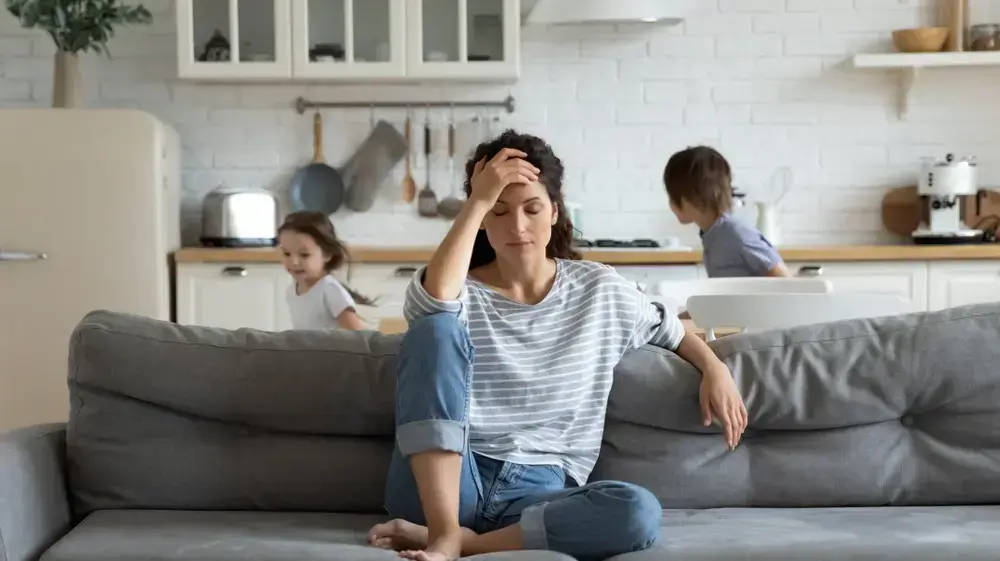 אמא מתוסכלת יושבת על הספה וילדים משתוללים סביבה