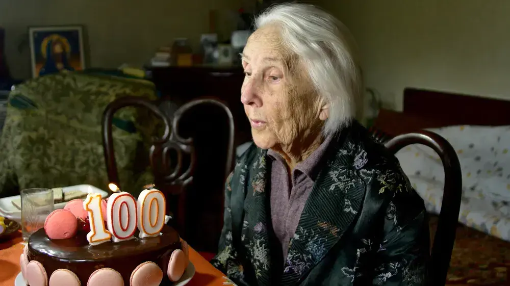 אישה זקנה מכבה נרות על עוגת יום הולדת בגיל 100 אישה זקנה מכבה נרות על עוגת יום הולדת בגיל 100