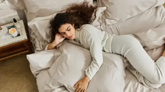 אישה שוכבת במיטה מסודרת עם מצעים