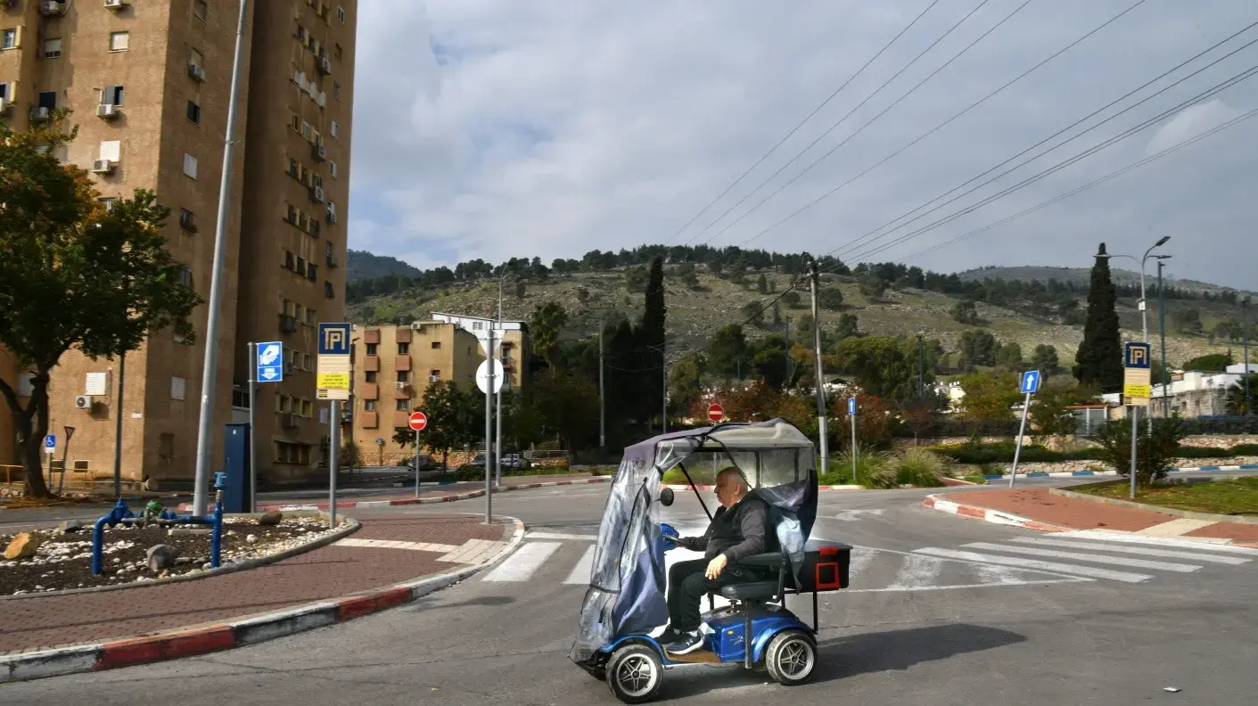 גבר נוסע על קלנועית וברקע דגל ישראל, קריית שמונה, 2 בינואר 2024