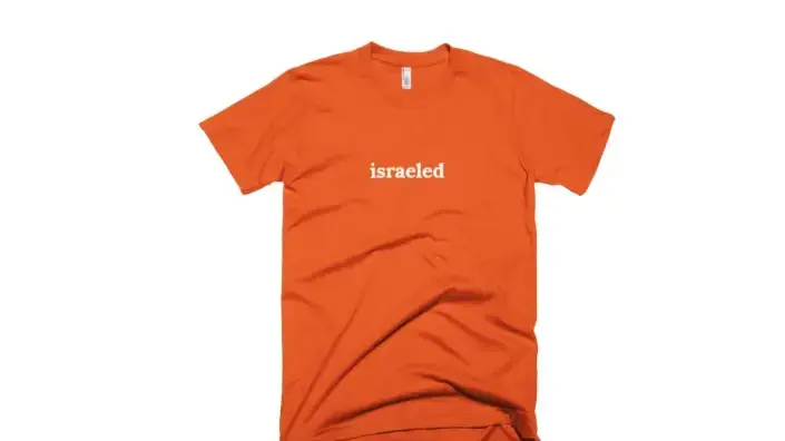 חולצה עם הכיתוב "Israeled" ומאחוריה ההגדרה האנטישמית.