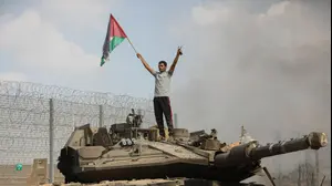 פלסטיני ליד טנק צה"ל שרוף קרוב לגדר הגבול עם חאן יונס, רצועת עזה, 7 באוקטובר 2023