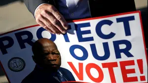 פעיל מחזיק שלט עם תמונתו של חבר הקונגרס המנוח ג'ון לואיס , עצרת מול בימ"ש העליון של ארה"ב, 15 באוקטובר 2025