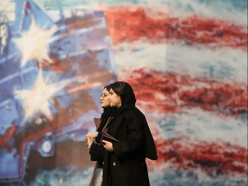 נשים חולפות על פני שלט אנטי-אמריקני בטהראן, איראן, 26 בינואר 2026